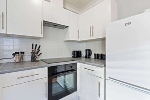 Une cuisine moderne avec des armoires blanches, un four noir et un réfrigérateur blanc.