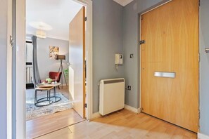 Un pasillo con una puerta de madera, un radiador y una pequeña mesa con una planta.