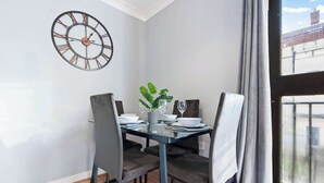 Un comedor con una mesa de vidrio, cuatro sillas, una planta en maceta y un reloj de pared.