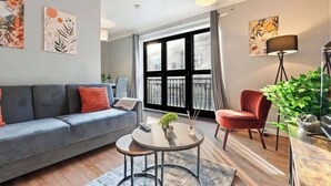 Ein modernes Wohnzimmer mit einer grauen Couch, einem roten Sessel, einem runden Couchtisch und einem großen Fenster mit Vorhängen.
