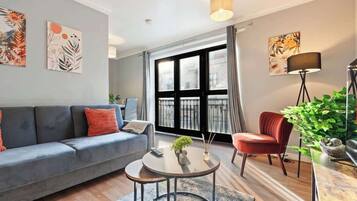 A modern living room with a grey sofa, a red armchair, a round coffee table, and a large window with curtains.