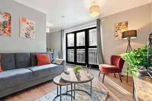 Una sala de estar moderna con un sofá gris, un sillón rojo, una mesa de centro redonda y un ventanal con cortinas.