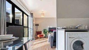 Una cocina moderna con lavadora y secadora integradas, un comedor con mesa de vidrio y una zona de estar acogedora con una silla roja.