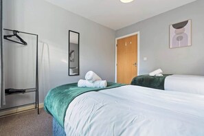 Habitación de hotel con dos camas, una puerta de madera, un espejo y un perchero.