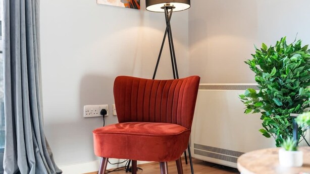 Ein roter Stuhl in einem Raum mit Stehlampe, Heizkörper und Topfpflanze.