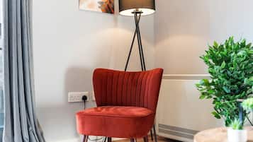 A red chair in a room with a floor lamp, a radiator, and a potted plant.