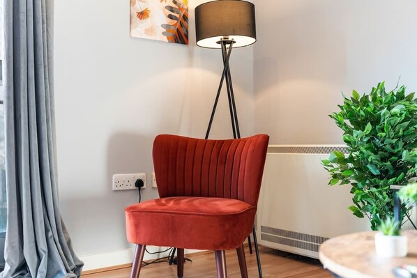 A red chair in a room with a floor lamp, a radiator, and a potted plant.