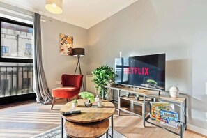 Una sala de estar moderna con un televisor de pantalla plana grande, una silla roja, una mesa de centro y una estantería con revistas.