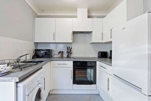 Una cocina compacta con armarios blancos, horno integrado, lavavajillas y microondas.