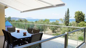 A balcony with a table and chairs, overlooking a coastal landscape with trees and the sea.
