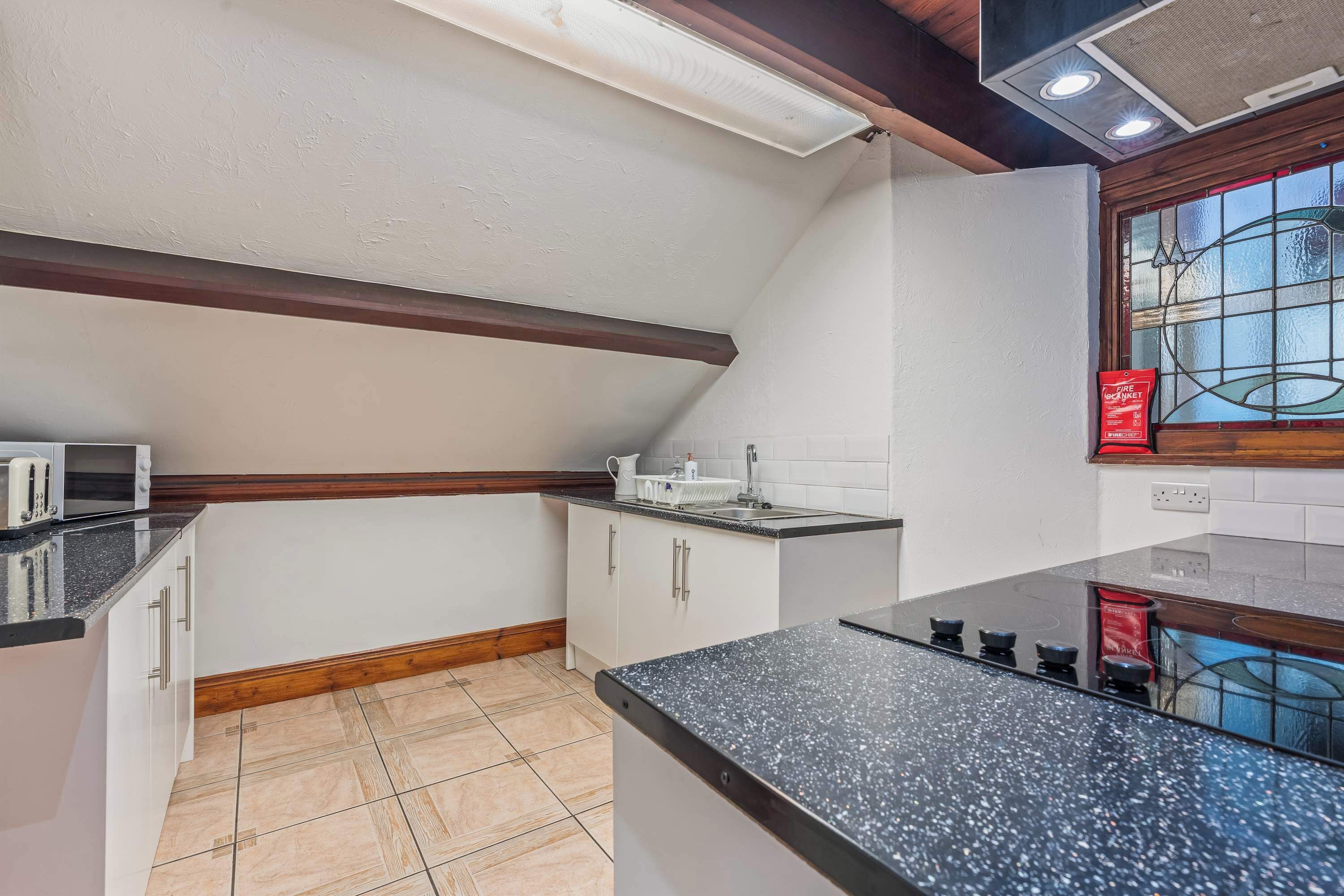 A kitchen with white cabinets, a black countertop, and a window with a red fire safety sign.