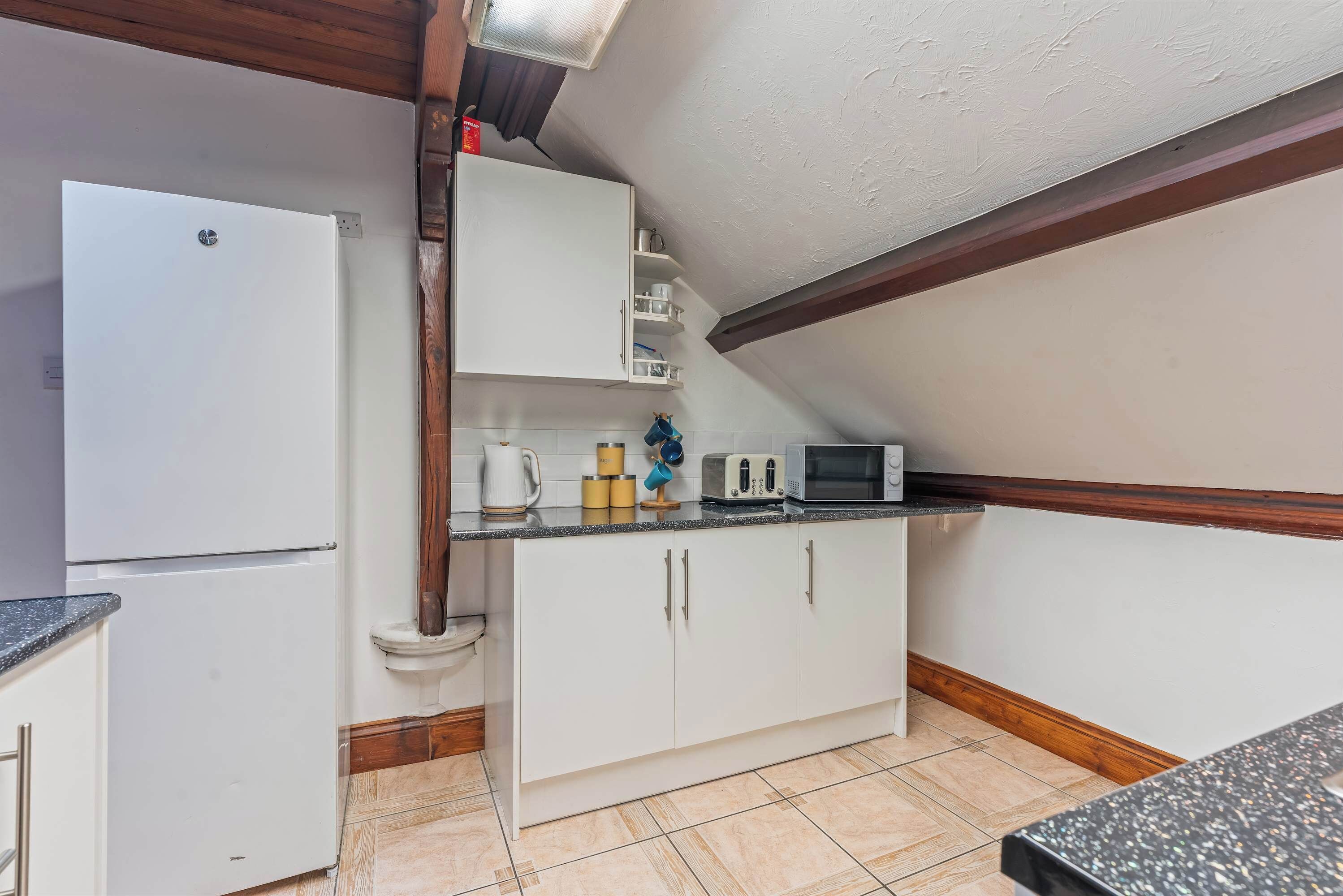 Una cocina con armarios blancos, un refrigerador blanco, un microondas y un tostador sobre la encimera.