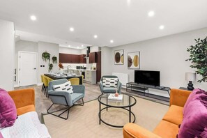 A modern living room with orange and blue sofas, a glass coffee table, and a flat-screen TV.