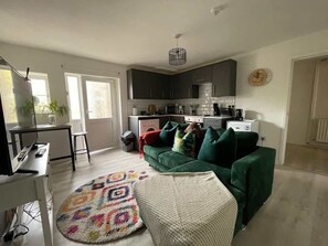 A modern living room with a green sofa, a patterned rug, and a kitchen in the background.