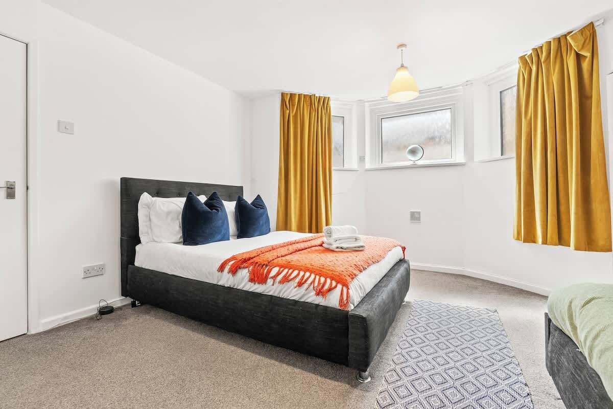 Une chambre à coucher avec un lit, une table de chevet, une fenêtre et des rideaux.