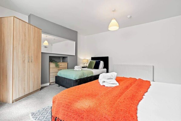 A modern bedroom with a large wardrobe, a bed with an orange blanket, a bedside table with a lamp, and a mirror on the wall.