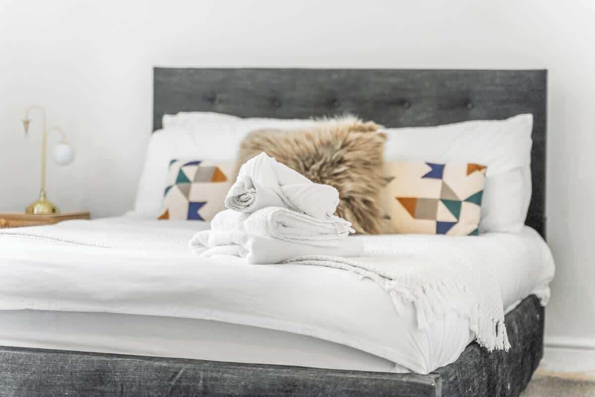 A neatly made bed with white linens, a fluffy pillow, and patterned pillows.