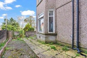 Un immeuble résidentiel avec une façade en pierre, une petite fenêtre et un chemin pavé menant à un jardin.