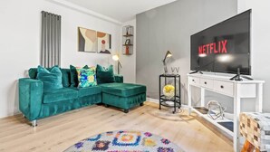 Una sala de estar moderna con un sofá color turquesa, una alfombra redonda, un mueble blanco para televisión y un televisor de pantalla plana grande mostrando