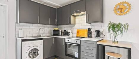 Una cucina funzionale con mobili grigi, un forno a microonde integrato, una macchina da caffè e una lavatrice.