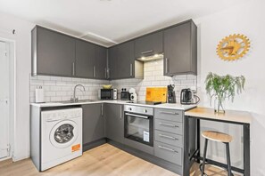 A compact kitchen with grey cabinets, a built-in microwave, a coffee maker, and a washing machine.