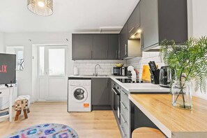 A modern kitchen with grey cabinets, a washing machine, and a wooden countertop.