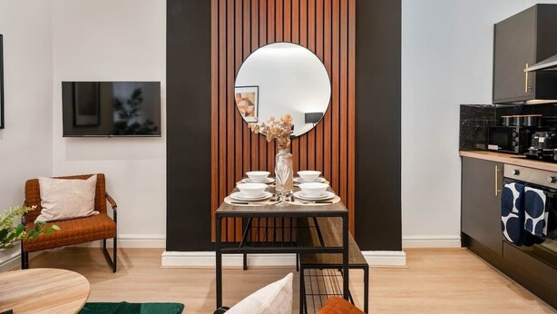 Een moderne keuken met een eetgedeelte, met een wand bekleed met hout, een ronde spiegel en een eettafel gedekt voor zes personen.