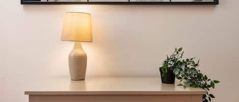 A minimalist room with a light-colored dresser, a wall-mounted mirror, a lamp, and a small potted plant.