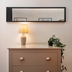 A minimalist room with a light-colored dresser, a wall-mounted mirror, a lamp, and a small potted plant. - Layla's Retreat Apt 4 - City Centre - Parking (Merseyside)