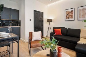 A modern living room with a black sofa, a dining table with chairs, and a kitchen area with dark cabinets. - Layla's Retreat Apt 4 - City Centre - Parking (Merseyside)