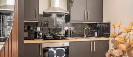 Una cocina moderna con armarios oscuros, una campana extractora de acero inoxidable, horno empotrado y encimera de mármol.