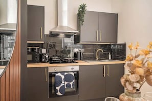 A modern kitchen with dark cabinetry, a stainless steel range hood, a built-in oven, and a marble countertop. - Layla's Retreat Apt 4 - City Centre - Parking (Merseyside)