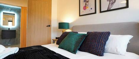 A hotel room with a bed, a nightstand, a lamp, and two framed artworks on the wall.
