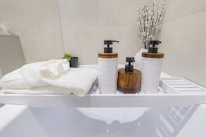 A bathroom with a white sink, two soap dispensers, a towel, and a small plant.