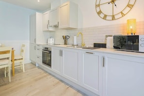 Une cuisine moderne avec des meubles blancs, une grande horloge murale, un évier avec un robinet doré et un four à micro-ondes.