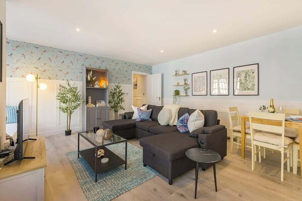 A modern living room with a sectional sofa, a dining table, and a kitchen area in the background.