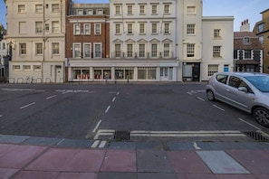 A street view with a row of buildings, including a row of shops with large windows and a car parked on the side.
