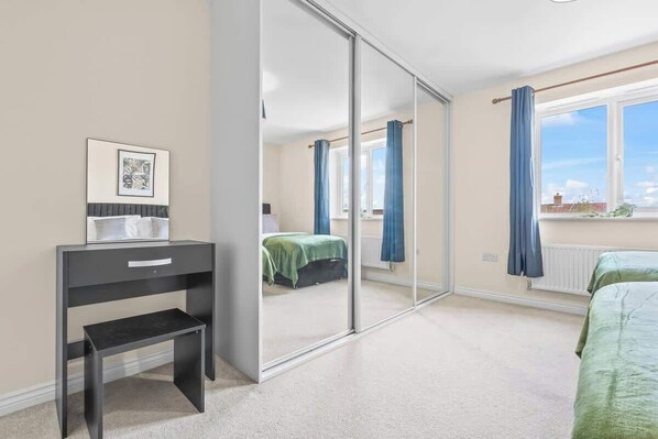 Une chambre avec une porte-fenêtre coulissante, un lit avec une literie verte, une table de chevet avec une lampe et un tableau encadré au mur.
