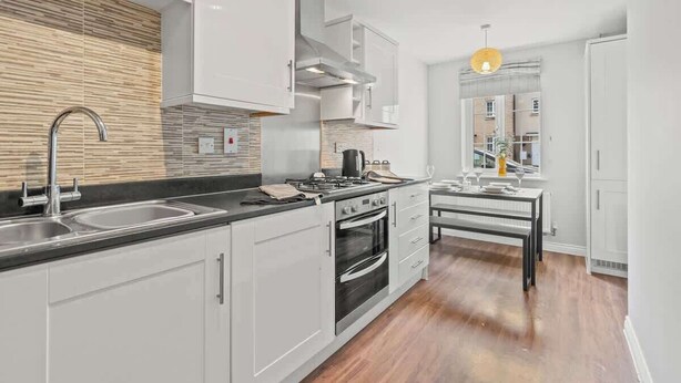 Une cuisine moderne avec des meubles blancs, un évier en acier inoxydable, une cuisinière à gaz et un four encastré.