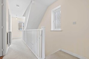 Un couloir avec une rambarde blanche, une fenêtre et une porte.