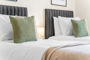 Un lit bien fait, avec une literie blanche et deux oreillers, un vert et un blanc, dans une chambre d’hôtel.