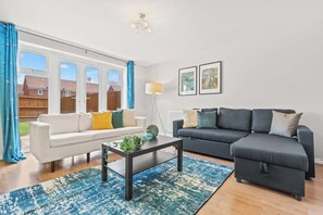 Un salon avec un canapé blanc, un canapé foncé, une table basse et un lampadaire. Deux tableaux encadrés sont accrochés au mur.