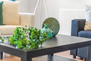 A modern living room with a dark wooden coffee table, a green glass vase, and a green plant. - Stylish 4 Bedroom House in St Neots w Free Parking (Cambridgeshire)