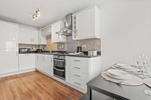 Une cuisine moderne avec des meubles blancs, un four encastré et un coin repas avec une table dressée pour quatre personnes.