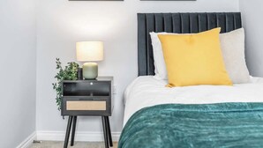 Une chambre à coucher bien rangée, avec un lit, une table de chevet, une lampe et deux tableaux encadrés accrochés au mur.