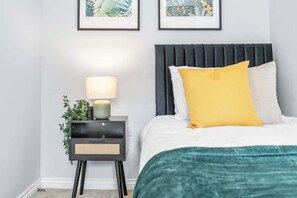A neatly arranged bedroom with a bed, bedside table, lamp, and two framed pictures on the wall. - Stylish 4 Bedroom House in St Neots w Free Parking (Cambridgeshire)