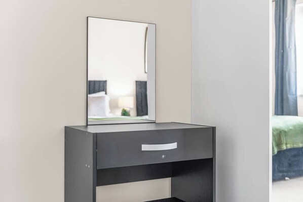 Une salle de bain moderne avec un grand miroir, un meuble-lavabo de couleur sombre et un lit vert visible à travers la fenêtre.