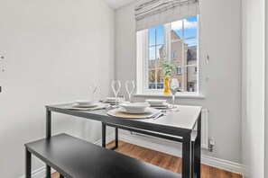 Un coin repas avec une table dressée pour quatre personnes, un banc et une fenêtre donnant sur des immeubles.