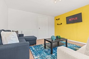 Una sala de estar con un sofá, una mesa de centro y un televisor de pared que muestra 'NETFLIX'.