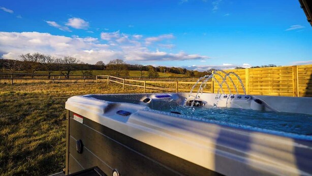 Un jacuzzi con vistas a un campo cubierto de césped y una valla de madera bajo un cielo despejado.